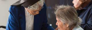 Nun assisting elderly woman in a wheel chair
