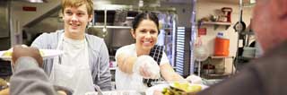 Two staff serving food in a homeless shelter kitchen