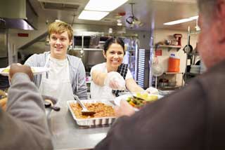 Two staff serving food in a homeless shelter kitchen