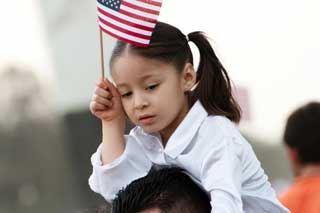 Young immigrant girl waving an American flag while riding on her father's shoulders