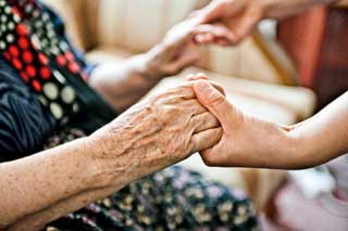 Close-up of an elderly person's hands being clasped in those of a younger person
