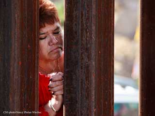 Woman praying at the border between the United States and Mexico