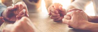 Several people sitting at a table with their hands clasped in prayer
