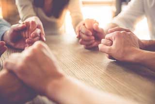 Several people sitting at a table with their hands clasped in prayer