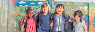 Four children linking arms and laughing in a schoolyard