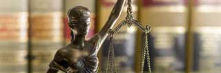 A statue of Lady Justice stands in front of a row of legal books