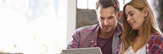 A man and a woman working together on a laptop while sitting on the couch at home