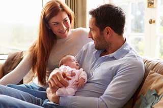 A husband and wife smile at each other while holding their newborn baby