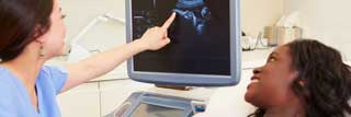 A nurse points to a screen showing an ultrasound image of an expectant mother's child