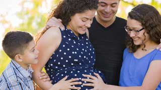 A smiling family consisting of a son, daughter, father, and expectant mother