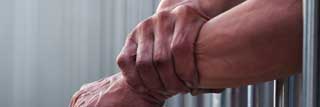 A young man's hands resting outside the bars of his jail cell