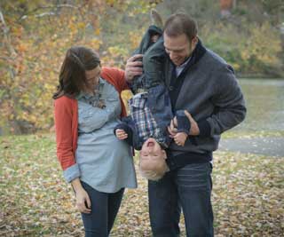 An expectant mother and her husband play with their son in the park on a fall day