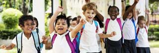 A group of Catholic school children, outside, laughing and running towards the viewer