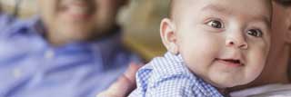 A small child smiles past the camera while being held by his mother