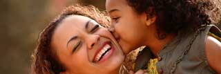 A young girl kisses her laughing and smiling mother on the cheek