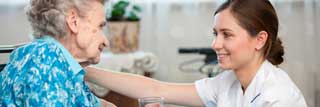 A young nurse smiles at an elderly woman in a wheelchair while handing her a glass of water
