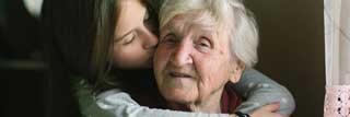 A young girl kissing a smiling elderly woman on the cheek