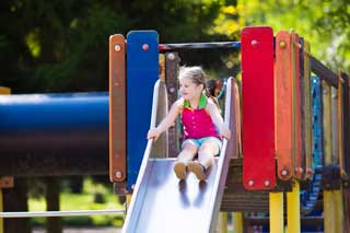 A young girl gets ready to go down a slide at the park