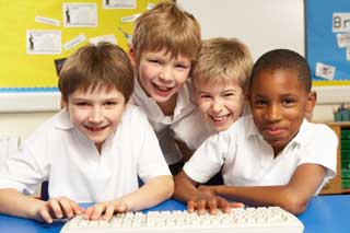 Four Catholic schoolchildren smile while sharing a computer keyboard