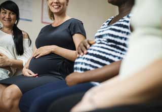 Several pregnant women, smiling and holding their bellies