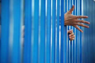 A juvenil's hands reaching through the bars of a jail cell