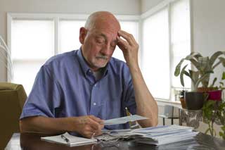 A man contemplates his overdue bills while holding his head in his hand