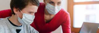 A student and teacher wearing masks, working together to solve a problem on a laptop