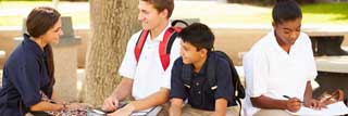 Four students in uniform sitting outside talking and doing homework.