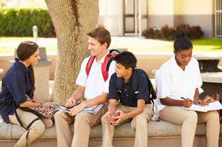 Four students in uniform sitting outside talking and doing homework.