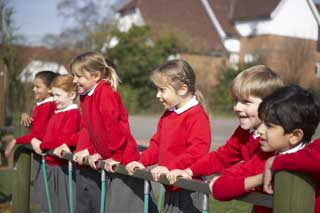 Six happy school children in uniform watching sports from behind a fence