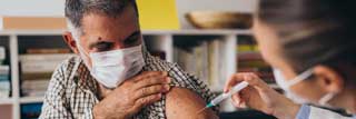 A man wearing a protective facemask receiving a vaccination shot from his doctor