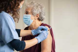 An elderly woman receives the COVID-19 vaccine from her health practitioner