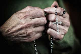 An elderly woman's hands praying the Rosary