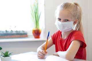 A young girl wearing a protective face mask while doing her school work.