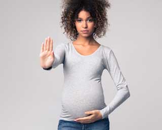 A pregnant woman holding her belly with one hand and holding the other up in a gesture meaning “stop”