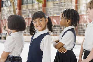 Four children in school uniforms standing in line. One girl smiles at the camera.