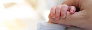 Closeup of a newborn baby’s hand grasping their parent’s thumb