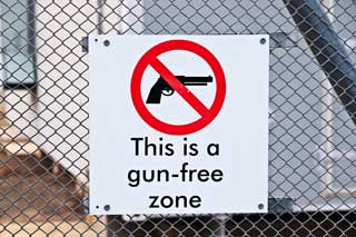 Sign reading “This is a gun-free zone” attached to a wire mesh fence