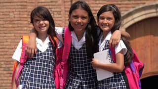 Three smiling girls in school uniforms with their arms around each other