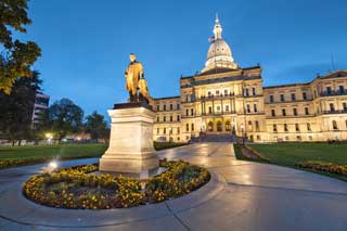 The exterior of the Michigan State Capitol building, lit up at dusk.