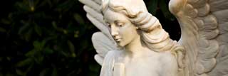 A angel carvel from marble, wings spread and holding a crucifix.