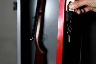 A hand preparing to close the door on a gun safe, thus locking a rifle inside.
