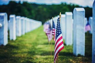 A row of American flags between two rows of white headstones.
