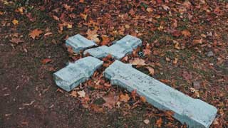 A broken cross laying in the grass, surrounded by dead leaves