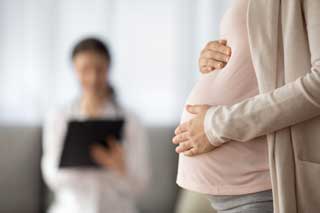 Close-up of a pregnant woman protectively holding her belly with both hands