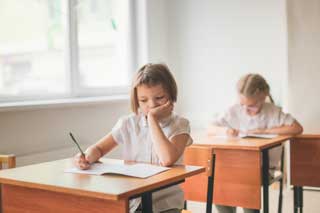 Two young girls in school uniforms taking a test in the classroom