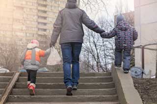 A father and his two children walking up a flight of stairs toward an appartment building