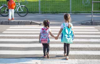 Two small children, holding hands as they prepare to cross the street.