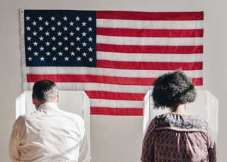 Two people with their backs to the camera voting against Proposal 3. An American flag hangs on the wall in front of them.