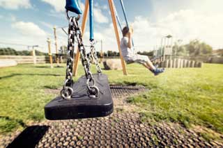 Empty swing in a children's playground, with a lone child in the background
